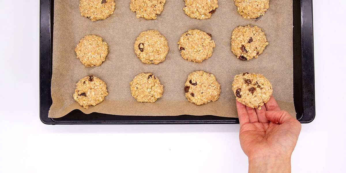 Der rund-geformte Rosinen-Hafer-Cookie-Teig wird per 16 Cookies auf ein Backblech getan.