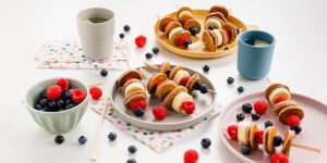 Pfannkuchen Spieße mit Himbeeren, Bananenscheiben & Blaubeeren auf Tellern