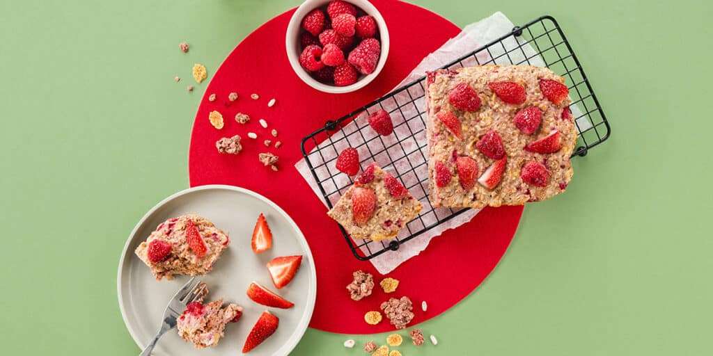 Frühstückskuchen auf einem Gitter. Daneben ist ein Stück Frühstückskuchen auf einem Teller serviert mit frischen Erdbeeren und Himbeeren als Dekoration.