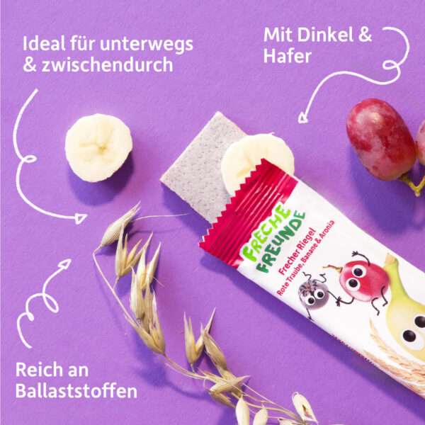 Ein aufgerissener Freche Freunde Bio Riegel Rote Traube, Banane & Aronia liegt auf lila Hintergrund. Neben ihm Banane, Trauben und Haferähren – mit Beschriftungen wie „Mit Dinkel & Hafer“, „Reich an Ballaststoffen“ und „Ideal für unterwegs & zwischendurch“.