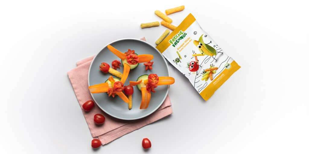 Gemüseblumen auf einem Teller serviert daneben liegt eine Packung Freche Freunde Knusper-Sticks