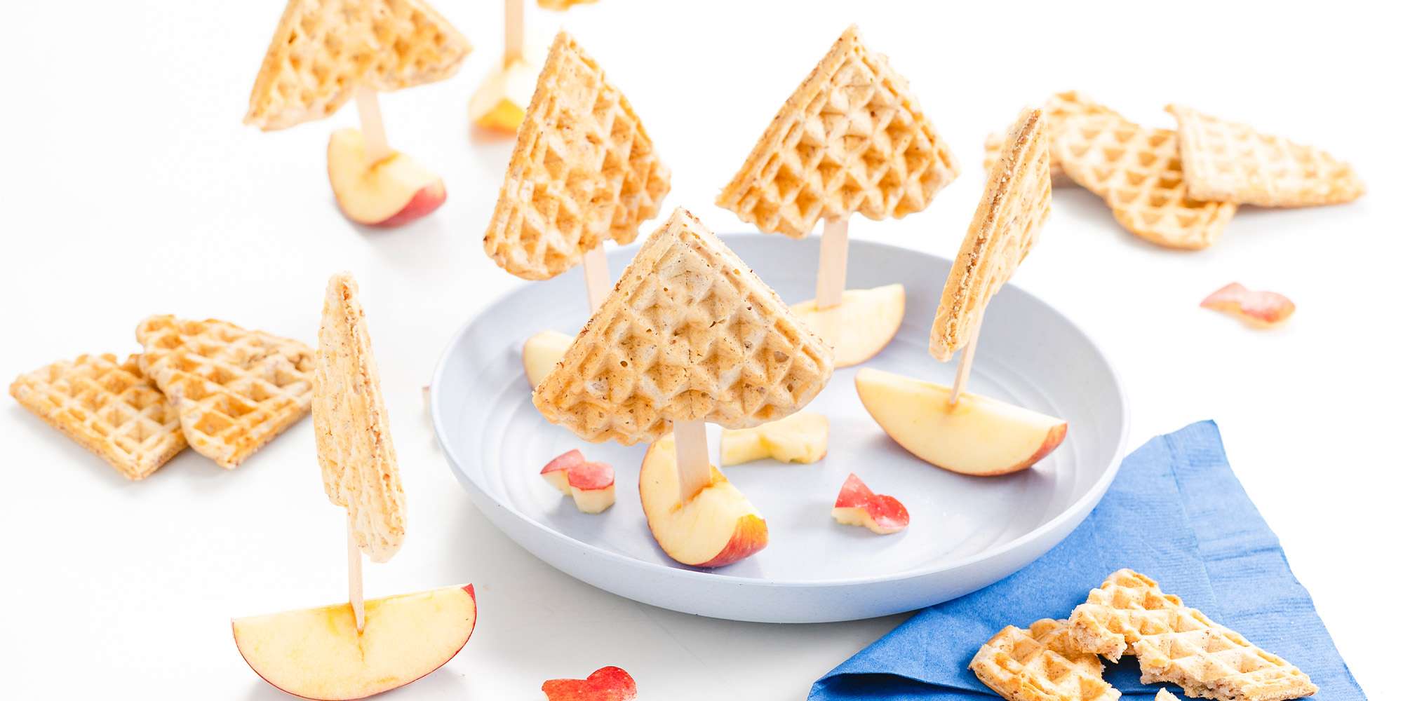 Freche Freunde - Rezept Waffeln am Stiel - Waffelschiffchen - jeweils eine Waffel auf einem Stäbchen, welches in einem Apfelstück steckt. Ein paar kleine Fische aus Apfel zerstreut.