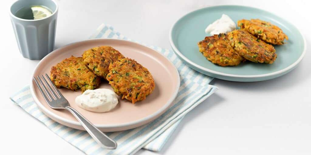 Zucchini Puffer auf Tellern serviert dazu ein Klecks Kräuterquark.