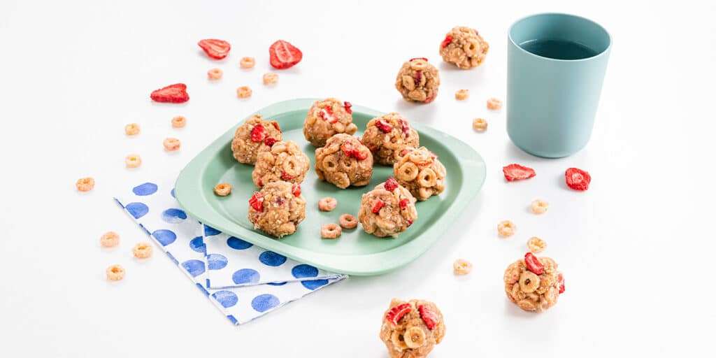 Energiekugeln mit Cerealien auf einem Teller serviert. Daneben steht ein Becher mit Wasser.
