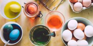 Weiße Eier liegen in Behältern mit gelben, blauen und rötlichem Farbsud für natürliches Färben