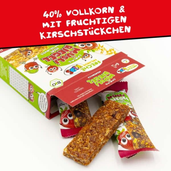 Eine geöffnete Packung Freche Freunde Bio Müsliriegel mit einem herausragenden Riegel – gut zu sehen sind die leckeren Fruchtstücke und Getreideflocken. Text: 40% Vollkorn & mit fruchtigen Kirschstücken.