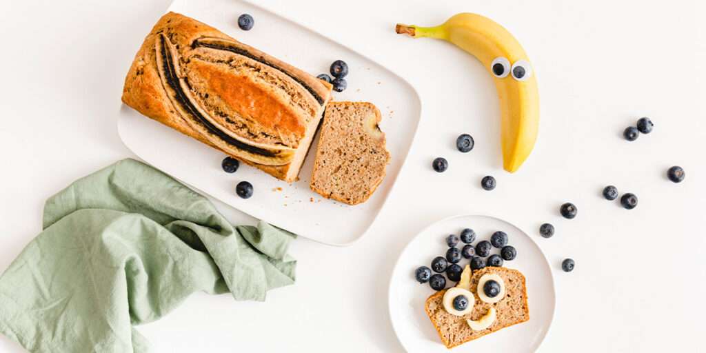 Bananenkuchen-ohne-Zucker und Banane mit Wackelaugen und Kuchenscheibe belegt mit Früchten wie ein Gesicht