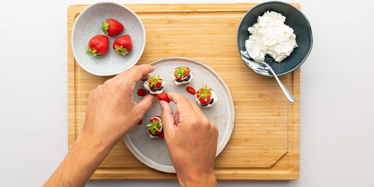 Die Erdbeer Zwerge bekommen Nasen mit kleinen Erdbeerstückchen und Augen mit Blaubeeren. Daneben die restlichen Erdbeeren und Quark.