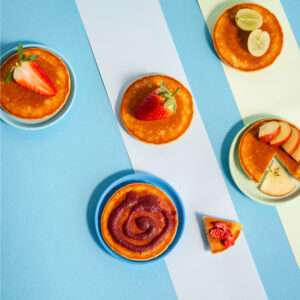 Pancakes angerichtet auf einem Teller mit Früchten auf blauem Hintergrund