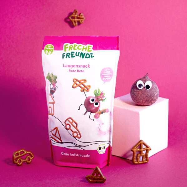 Freche Freunde Bio Laugensnack Rote Bete – rosa inszeniert mit knusprigen Mini-Brezeln in Fahrzeug- und Hausformen. Rosalie Rote Bete thront frech mit Kulleraugen auf einem Podest.