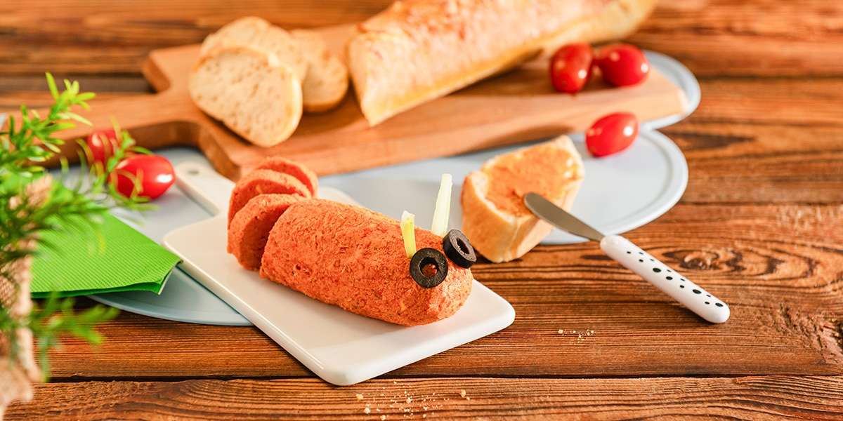 Tomatenbutter auf einem Teller serviert, mit Olivenscheiben als Augen, dazu Baguette