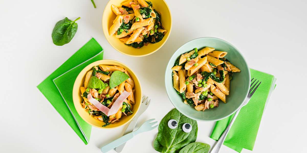 One Pot Spinat Pasta in 3 Tellern angerichtet und mit Schinken dekoriert. Frischer Spinat liegt als Deko nebenbei sowie Besteck.