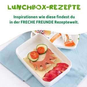 Lunchbox mit belegtem Brot in Löwenform aus Käse, Wurst, Tomate und Gurke. Daneben aufgeschnittene Apfelschnitze. Im Hintergrund eine Packung des Freche Freunde Riegels. Text: „Lunchbox-Rezepte – Inspirationen wie diese findest du in der Freche Freunde Rezeptwelt“.