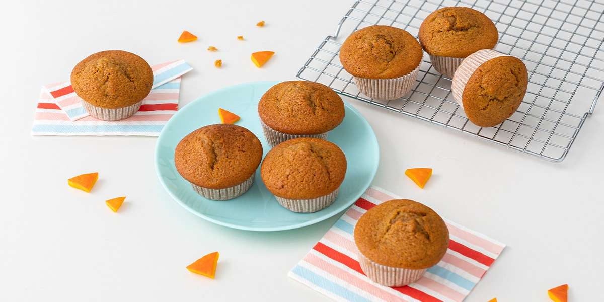 Kürbismuffins auf einem Teller serviert. Daneben liegen noch weitere Kürbismuffins auf einem Gitter zum Abkühlen.