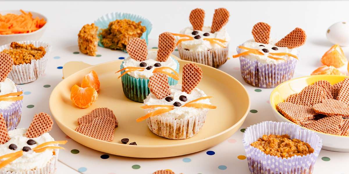 Ostermuffins mit Osterhasengesicht auf einem Teller serviert. Waffeln stecken als Osterhasenohren in den Muffins.
