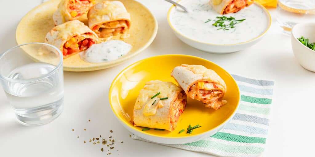 Wrap Pizzaschnecken auf zwei Tellern serviert. Dazu ein Joghurt Dip in einer Schüssel und ein Glas Wasser.