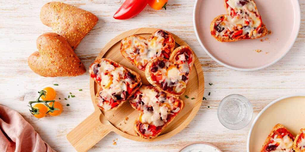 Überbackende Pizzabrötchen liegen auf einem Bett in der Mitte. Daneben zwei Teller mit Pizzabrötchen serviert und Kräuterdip in einer Schüssel.