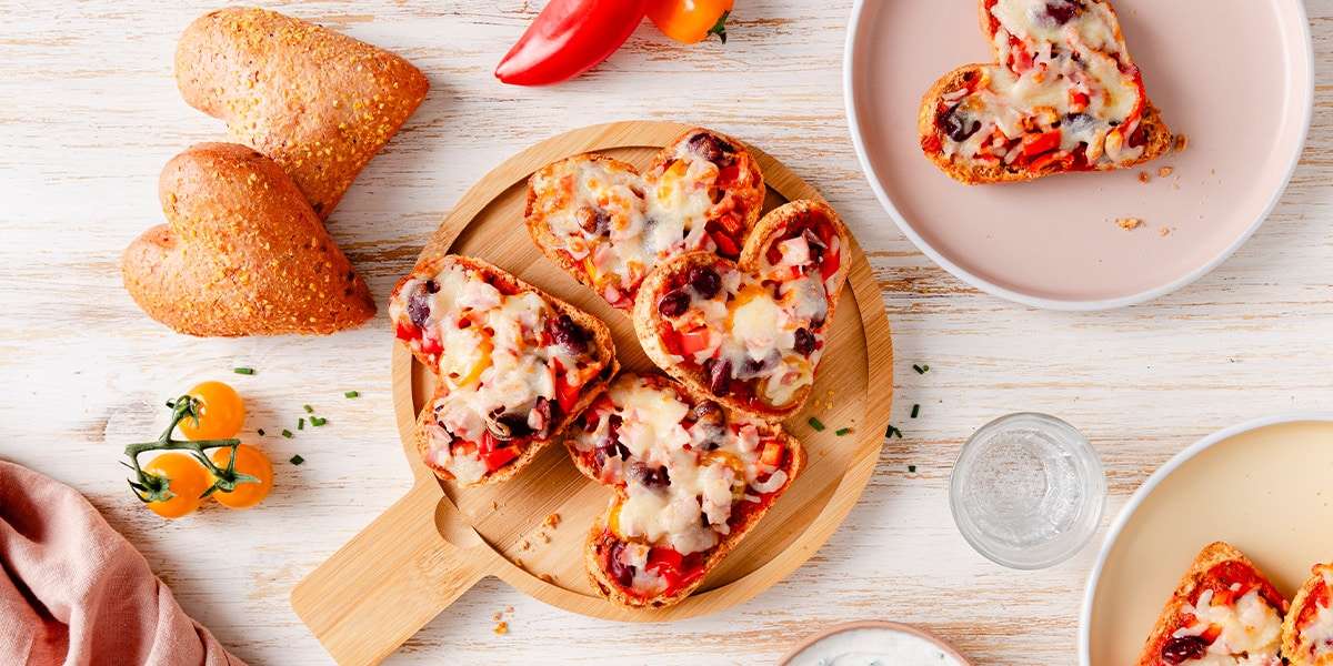 Überbackende Pizzabrötchen liegen auf einem Bett in der Mitte. Daneben zwei Teller mit Pizzabrötchen serviert und Kräuterdip in einer Schüssel.